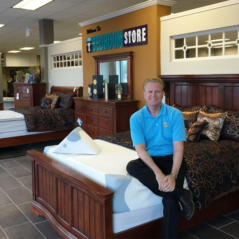 Denny Boyd, owner of the Bedroom Store, sitting on mattress inside a Bedroom Store location